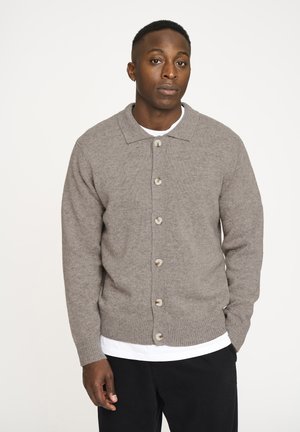 Grå uld cardigan med krave, syv store knapper, ribbede manchetter og lige søm, parret med en hvid T-shirt under.