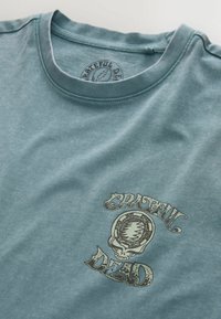Blaues Grateful Dead T-Shirt mit Totenkopf- und Blitzlogo, das in Brusthöhe gedruckt ist, und einem runden Halsausschnitt.