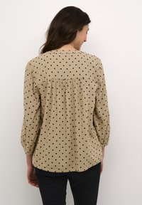 Beige blouse met polka dots, voorzien van driekwart ballonsmouwen, plooien op de rug en een afgeronde zoom, gemaakt van lichte stof.