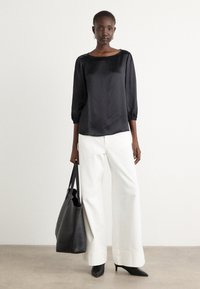 Zwarte satijnen blouse met driekwart pofmouwen, gecombineerd met witte wijde broek en een zwarte tote bag. Puntige zwarte hakken maken de look af.
