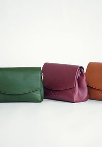 Drei Lederhandtaschen: dunkelgrün, burgunderrot und braun. Jede verfügt über einen Klappenverschluss, dezente Nähte und eine glatte Textur.