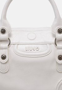 Borsa sintetica bianca con finitura testurizzata, accessori circolari, manici superiori e un'etichetta con la scritta "LIUJO."