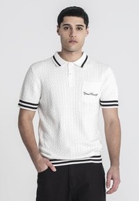 Polo blanco de punto trenzado con puños y cuello a rayas negras. Presenta un bolsillo delantero con detalle bordado. Diseñado para un ajuste ceñido.