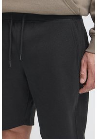 Shorts noirs en mélange de coton avec une taille élastique et des cordons de serrage, des poches latérales et une texture lisse. Aucun motif ni accent visible.