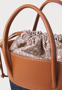 Brown leather handbag with a gathered, patterned fabric liner and curved handles. The texture is smooth, and the interior features a logo design.