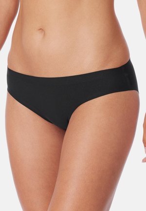 Woman's midsection wearing plain black hipster-style underwear against a white background.