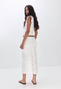 Bílý krajkový crop top a midi sukně, s přiléhavým střihem, květinovým vzorem a hladkou strukturou, nošeno s plochými černými sandály.