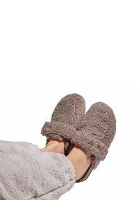 Cozy brown fuzzy slippers with a textured exterior, adjustable strap, and soft lining, paired with a light gray blanket.