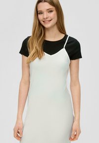 Robe nuisette blanche à couches avec des fines bretelles sur un haut à manches courtes noir. Texture lisse, design ajusté, look décontracté et accents simples.