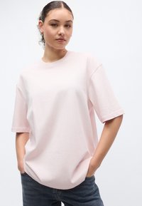 Ροζ ανοιχτόχρωμο μπλουζάκι σε oversized γραμμή από απαλό βαμβάκι με κοντά μανίκια. Διαθέτει στρογγυλή λαιμόκοψη και χαλαρή εφαρμογή, συνδυασμένο με σκουρόχρωμα τζιν.