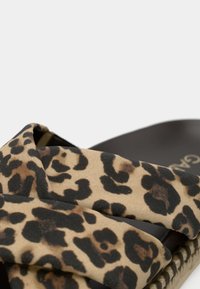 Σανδάλι με λουράκια και υφασμάτινο σχέδιο λεοπάρ διασχίζοντας μαύρη σόλα, που δείχνει λεπτομερή υφή και ραφές στο πλάι της σόλας.