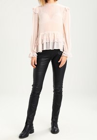 Jasnoróżowa bluzka z falbanami, posiadająca teksturowany wzór, warstwowy dół i długie rękawy. W połączeniu z dopasowanymi czarnymi skórzanymi spodniami i botkami za kostkę.