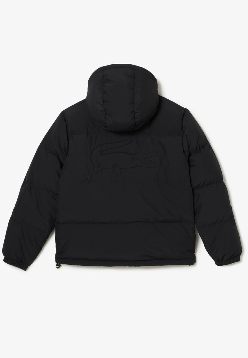 Doudoune noire avec capuche, présentant un design matelassé, des poignets élastiques et un logo Lacoste texturé au dos.