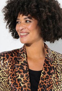 Leopardmönstrad blazer med glänsande yta, som har en blandning av bruna, svarta och gula nyanser. Strukturerade slag och en smal silhuett.