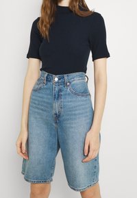 Top corto a maniche corte a coste scure abbinato a pantaloni bermuda in denim azzurro chiaro a vita alta, con chiusura a bottone e tasche anteriori.