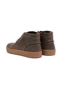 Bottes chelsea en cuir marron avec une semelle en caoutchouc texturé, dotées de coutures contrastantes et d'un col rembourré. La vue arrière montre un accent de languette.