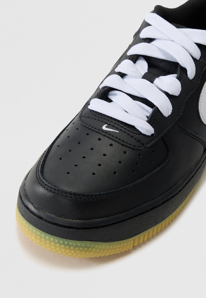 Schwarze Leder Sneakers mit weißen Schnürsenkeln, durchgehend perforierter Zehenbereich, hervorgehobenes Nike-Logo und durchsichtige Gummisohle. Glatte Textur mit genähten Details.