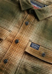 Camicia di flanella con un motivo a quadri marrone, verde e crema, con bottoni neri e un'etichetta che recita "Superdry Co Machined."