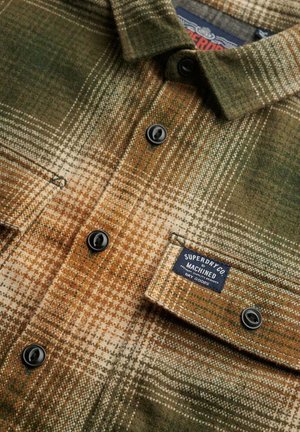 Chemise en flanelle avec un motif à carreaux marron, vert et crème, dotée de boutons noirs et d'une étiquette indiquant "Superdry Co Machined."