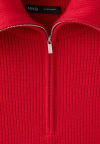 Gros plan d'un pull tricoté rouge à côtes avec une demi-fermeture éclair argentée et une étiquette noire indiquant MNG en taille small.