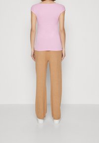 Pink short-sleeve top paired with beige wide-leg pants and white sneakers, viewed from the back against a neutral background.
