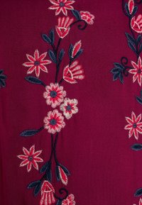 Głęboki burgundowy materiał z misternym haftem kwiatowym w odcieniach różu, kremu i granatu, z różnorodnymi kształtami kwiatów i akcentami liściastymi.