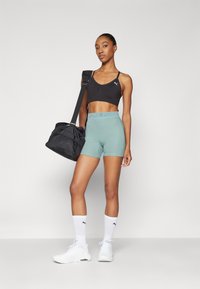 Completo sportivo composto da un reggiseno sportivo nero, pantaloni corti azzurri chiari con logo in vita, scarpe da ginnastica bianche e una borsa a tracolla nera.