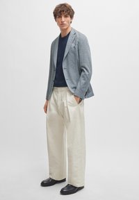 Blazer i blå og hvit hundetannmønster, sammen med en navy crew neck skjorte og kremfargede vidde bukser. Svarte sko, minimal detaljering.