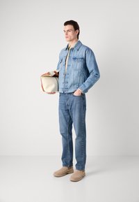 Denim jacket in light blue, beige shirt underneath, blue jeans, and tan boots. Holding a beige bag with brown accents. Simple, casual ensemble.