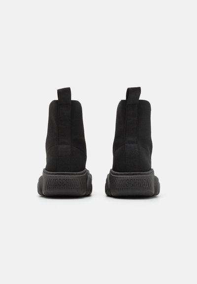 Black high-top sneakers with a stretchy fabric upper and chunky rubber sole. Features a logo detail on the heel and pull tabs at the back.
