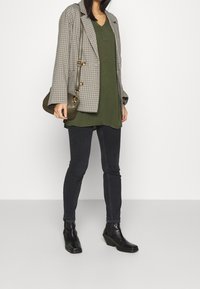 Kratkowana marynarka, oliwkowy top, ciemne skinny jeans, czarne botki za kostkę i mała oliwkowa torebka na ramię. Teksturalne materiały, warstwowy strój.