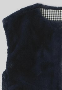 Gilet en fausse fourrure bleu marine foncé avec une surface texturée et un design sans manches ; l'intérieur présente un revêtement à carreaux noir et blanc.