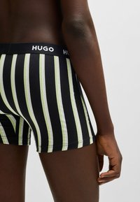 Schwarz-grün gestreifte Boxershorts mit einem HUGO-Logo-Bund, die ein enges Design und eine glatte Stoffoberfläche aufweisen.