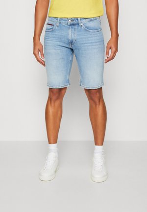 Shorts de mezclilla azul claros con un acabado ligeramente desgastado, corte recto y dobladillo deshilachado. Combinados con zapatillas blancas y calcetines cortos.