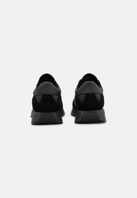 Black athletic shoes featuring a mix of smooth and textured materials, with a low-profile design and supportive rubber soles.