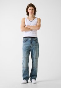 Jasnoniebieskie dżinsy z denimu z wzorem patchwork, prostym krojem nogawek i subtelnym przecieraniem. W połączeniu z dopasowanym białym topem na ramiączkach i białymi trampkami.