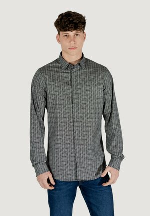 Camicia a maniche lunghe con bottoni in tessuto a fantasia bianco e nero, caratterizzata da un colletto a punta e una vestibilità rilassata, abbinata a jeans in denim blu.
