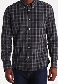 Uomo che indossa una camicia a maniche lunghe slim-fit a scacchi neri e grigi, abbinata a jeans blu scuro.