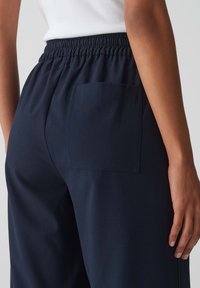 Un pantalon de survêtement bleu marine avec une taille élastique, une texture douce et une poche plaquée à l'arrière. Détails de couture visibles sur la poche.