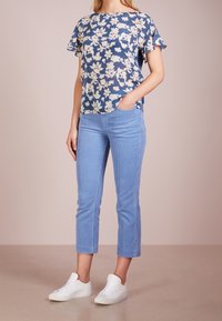 Top azul con estampado floral y mangas cortas con volantes, combinado con pantalones cortos de corduroy azul claro y zapatillas blancas sobre un fondo claro.