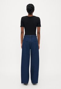 Schwarzes geripptes T-Shirt mit kurzen Ärmeln, kombiniert mit hochtaillierten, weiter geschnittenen dunkelblauen Jeans. Hat einen schlichten Rücken mit zwei Taschen.