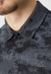 Černé polo tričko s texturovaným vzorem, s límečkem na knoflíky a vyšitým logem na hrudi. Měkká tkanina s moderním designem.