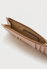 Ροζ δερμάτινο πορτοφόλι με φερμουάρ, εσωτερική θήκη για κάρτες και χρυσές λεπτομέρειες. Υφασμάτινη εξωτερική επιφάνεια με οριζόντιες ραφές.