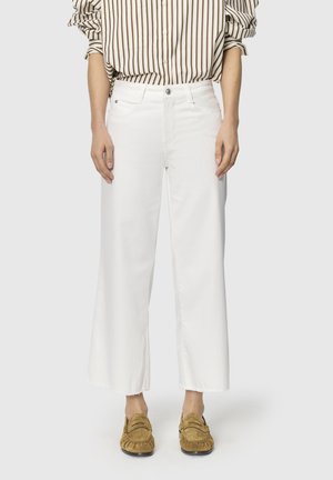 Persona vistiendo jeans blancos de talle alto y pierna ancha con dobladillos deshilachados, una camiseta de manga larga a rayas metida por dentro y mocasines marrones.