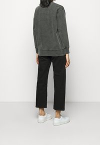 Sudadera gris con un acabado texturizado, con escote redondeado, mangas largas y puños acanalados, combinada con pantalones negros recortados y zapatillas blancas.