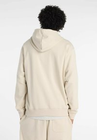 Felpa con cappuccio di un leggero beige, dal tocco morbido, con polsini a coste e vestibilità rilassata. Design semplice, cuciture visibili alle giunture.