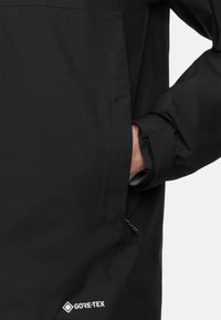 Czarna wodoodporna kurtka wykonana z materiału Gore-Tex, z boczną kieszenią i regulowanymi mankietami. Tekstura wydaje się gładka i trwała.
