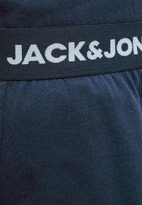 A sötétkék short anyaga vastag fekete derékrésszel rendelkezik, amelyen fehér "JACK & JONES" felirat található, sima textúrával és sportos dizájnnal.