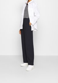Camisa blanca de botones sobre una camiseta de rayas en blanco y negro, combinada con pantalones anchos navy y zapatillas blancas.