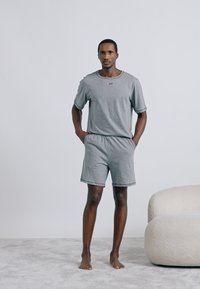 Σετ από γκρι κοντομάνικη μπλούζα από βαμβακερό μείγμα και σορτς με στρογγυλή λαιμόκοψη και ελαστική μέση, παρουσιάζεται σε όρθιο ανδρικό μοντέλο.